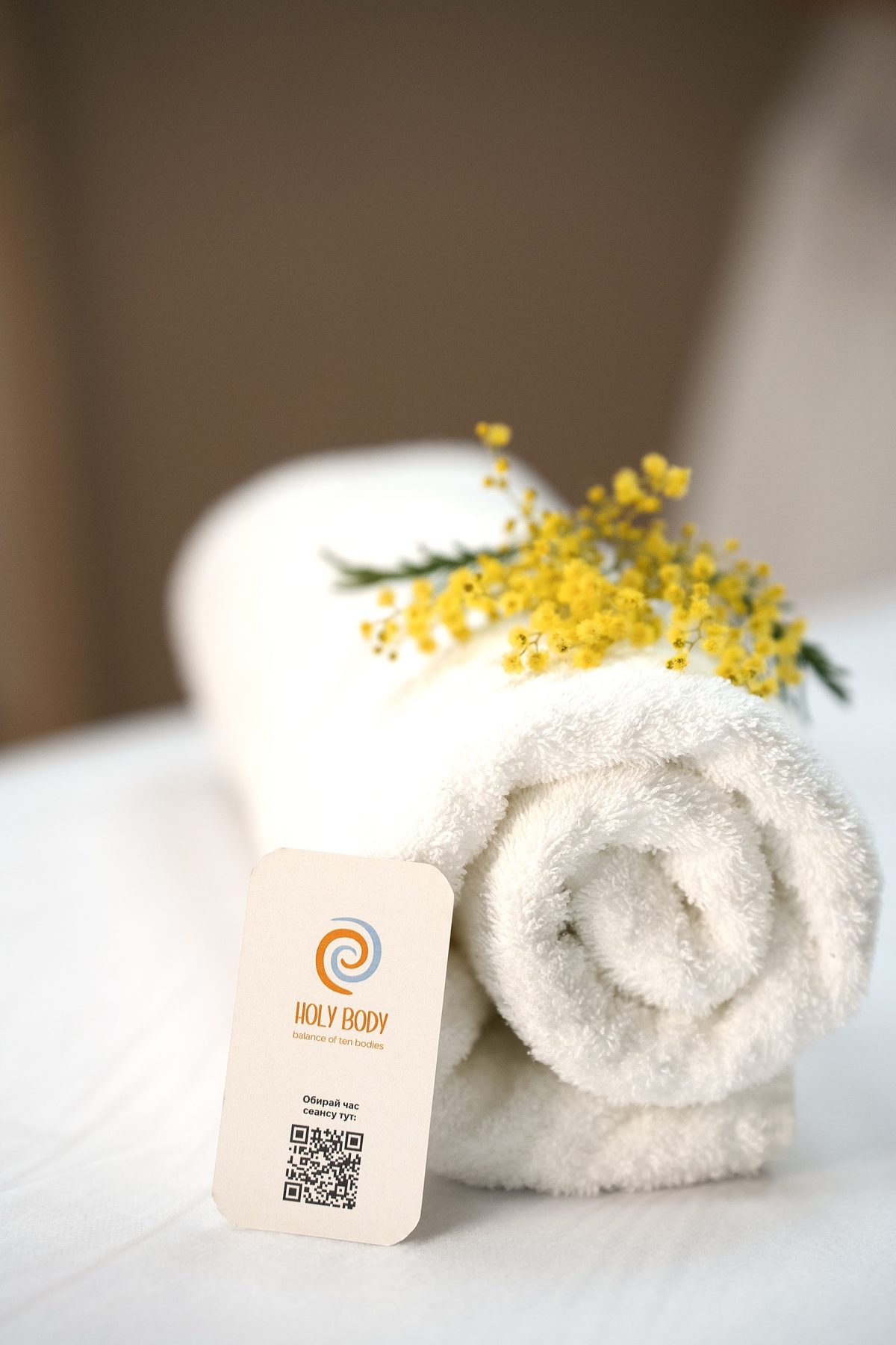 Opgerolde handdoek met mimosa en het visitekaartje van Holy Body
